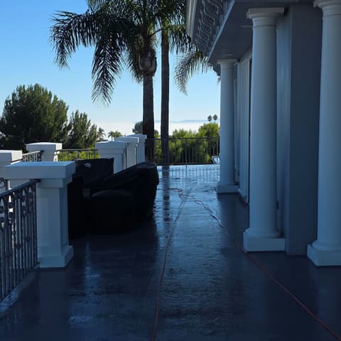 A columned balcony after pressure washing, the wet floor shining under the palms