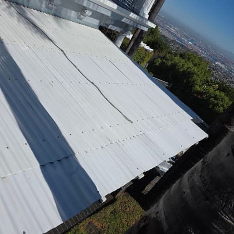A corrugated metal roof washed clean beside a balcony railing, valley view beyond