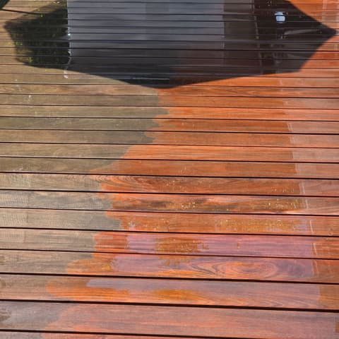 A hardwood deck half pressure-washed, the cleaned boards glowing beside the weathered ones