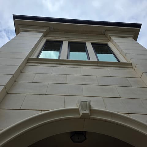 Looking up at a cleaned upper-storey window above an arched limestone entry