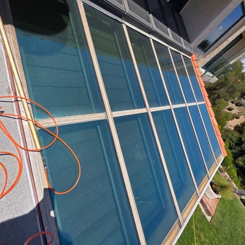 A bank of tinted glass panels on a hillside home, freshly cleaned, hose laid alongside