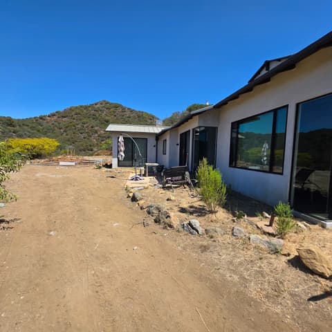 The side of a new hillside home, its picture windows cleaned, dirt drive alongside