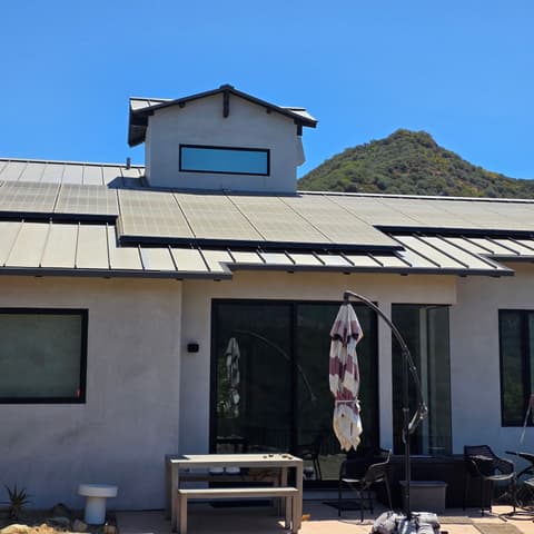 A single-storey home with a standing-seam roof and dark window frames, glass cleaned, patio furniture out front