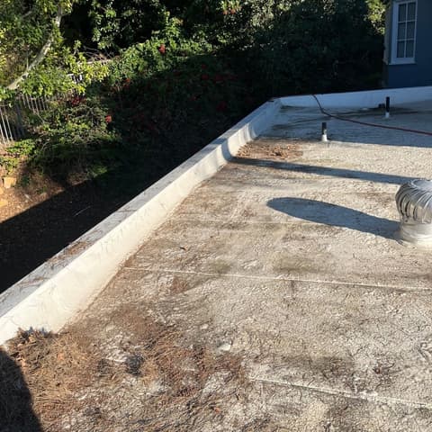 A flat roof section before cleaning, grey with debris gathered in the corner